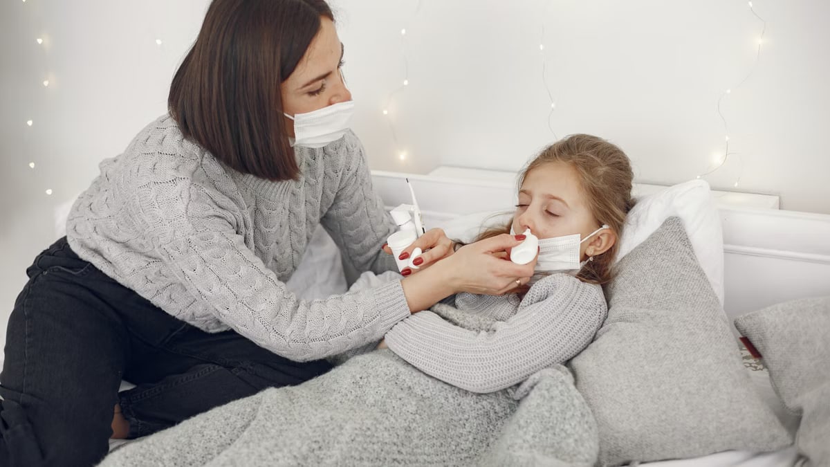 Mother administering nose drops to her sick daughter in a cozy bedroom setting.
